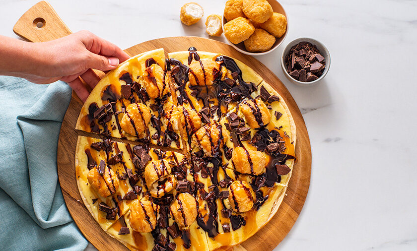 Choco-Caramel Cheesecake Pizza topped with chocolate pudding, caramel drizzle, chocolate chunks and cheesecake bites on a sliced dessert pizza crust.