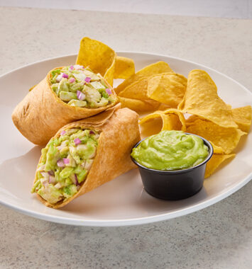 Avocado chicken salad wraps served with tortilla chips and a side of creamy guacamole-style dip.