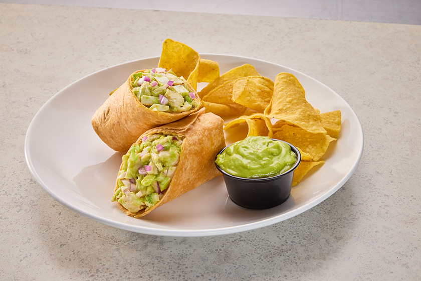 Avocado chicken salad wraps served with tortilla chips and a side of creamy guacamole-style dip.
