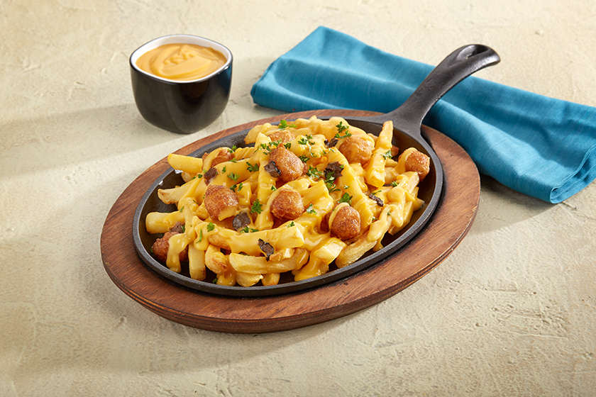 Poutine-Style Truffle Fries topped with Muy Fresco cheddar cheese sauce, crispy potato bites and fresh herbs, served in a cast-iron skillet.