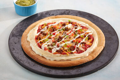 Mexican-style cheese burst pizza with layered tortilla, seasoned meat, peppers, cheese sauce drizzle and green onion on a black serving plate.